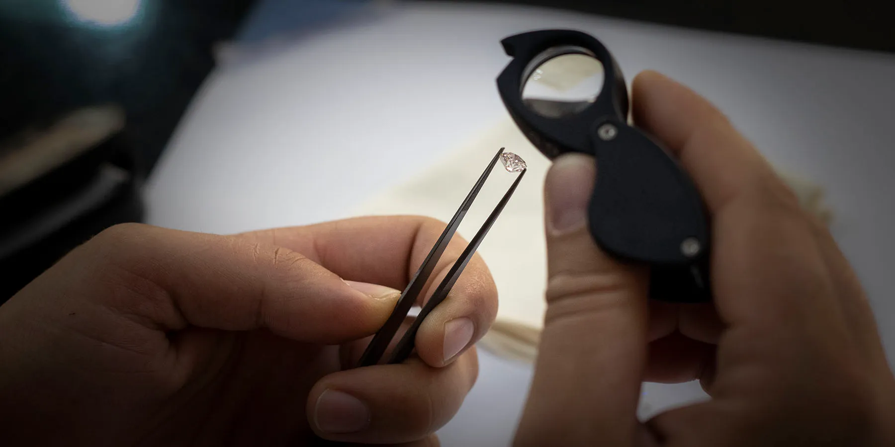 A grader examining a diamond with tweezers and a loupe